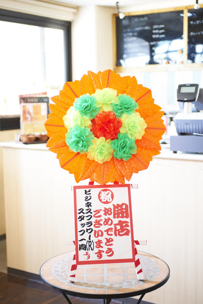 インパクト抜群の造花ミニ花輪（赤）は新装開店祝いにぴったりです。
