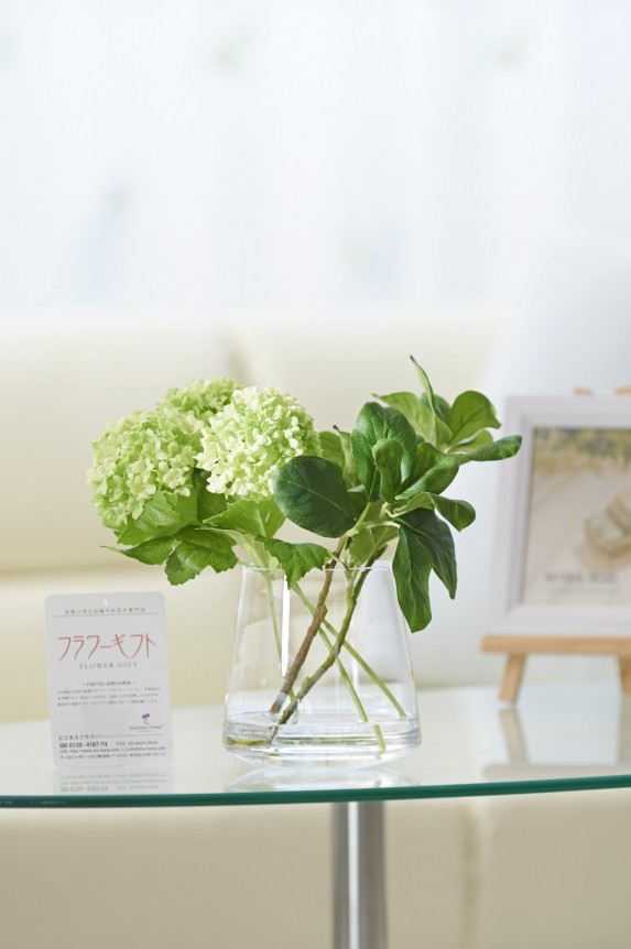 まるで水を注いだかのような花器に、淡く爽やかな色合い、アジサイに似た見た目で人気の植物「ビバーナム・スノーボール」を仕立てたアーティフィシャルフラワー（造花アート）商品です。