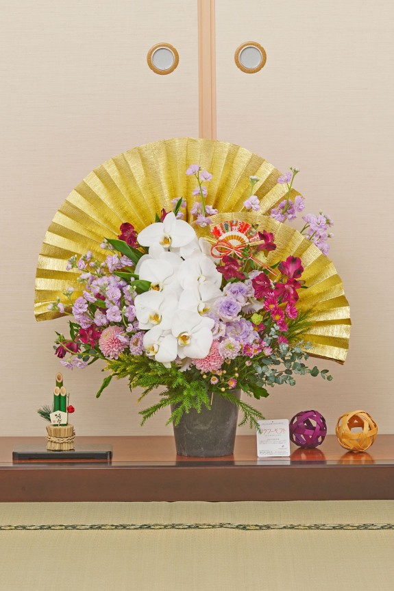 大きな黄金の扇飾りが目に留まる、新春飾りに相応しい豪華な紫系のアレンジメントフラワーです。