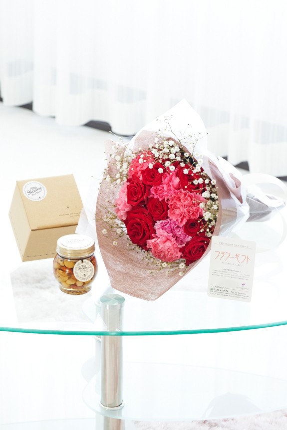 母の日の定番カーネーション＆皇室献上、農林水産大臣賞の受賞実績のあるバラ農園のバラをミックスさせた花束・ブーケに「いつもありがとう」の3D立体ピックを挿したお花と、ハンガリー大使館認証を受けたハンガリー産アカシアはちみつにこだわりのミックスナッツを漬け込んだナッツの蜂蜜漬けをセットにしたフラワーギフト用の商品です。