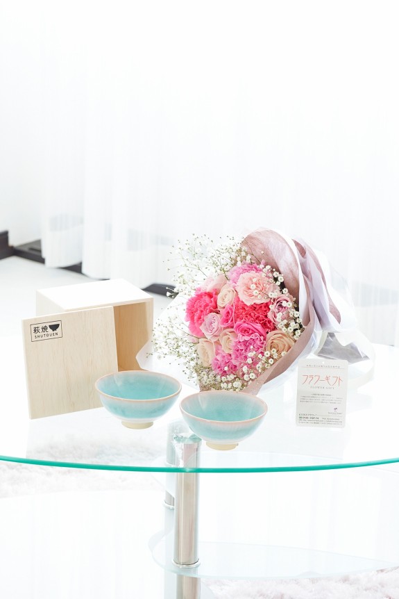 母の日の定番カーネーション＆皇室献上、農林水産大臣賞の受賞実績のあるバラ農園のバラをミックスさせた花束・ブーケに「いつもありがとう」の3D立体ピックを挿したお花と、すっきりとしてスマートなデザインで老若男女を問わない萩焼のペアお茶碗をセットにしたフラワーギフト用の商品です。