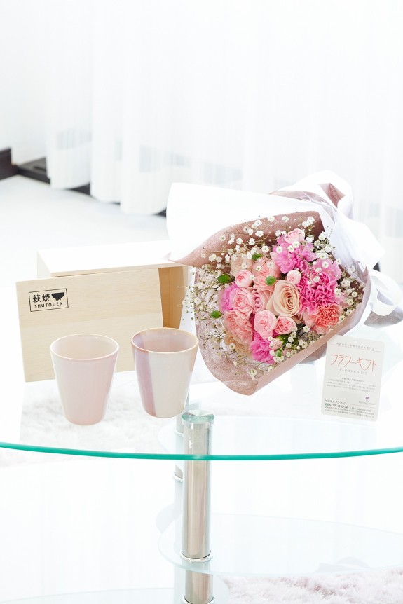 母の日の定番カーネーション＆皇室献上、農林水産大臣賞の受賞実績のあるバラ農園のバラをミックスさせた花束・ブーケに「いつもありがとう」の3D立体ピックを挿したお花と、すっきりとしてスマートなデザインで老若男女を問わない萩焼のペアカップをセットにしたフラワーギフト用の商品です。