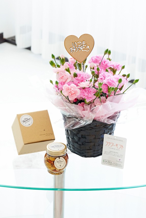 母の日の贈り物の定番でもあるカーネーションに、「いつもありがとう」の3D立体ピックを挿した鉢植えとこだわりのミックスナッツを漬け込んだナッツの蜂蜜漬けをセットにしたフラワーギフト用の商品です。