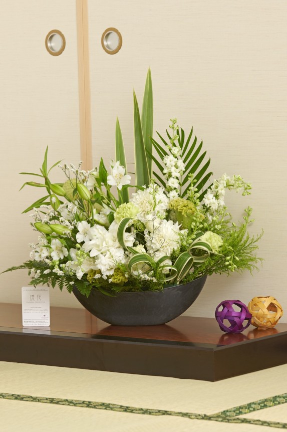 お洒落でスマートな花器に、白＆グリーンの花材で仕立てたデザイナーズ供花アレンジメント商品です。