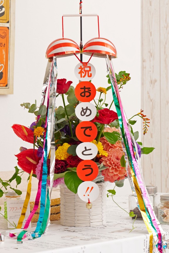 お祝いのシーンを盛り上げる存在感のあるくす玉が付いた、思わず目に留まる派手なアレンジメントフラワーです。