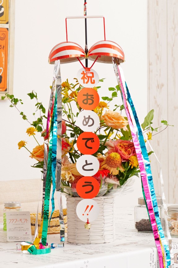 お祝いのシーンを盛り上げる存在感のあるくす玉が付いた、思わず目に留まる派手なアレンジメントフラワーです。