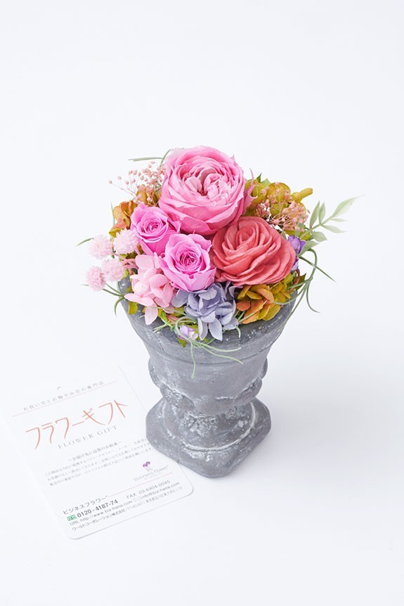 <p>木の皮で作られたソーラーローズなどの花材を、重厚感のある陶器の花器に仕立てた上品で温かみのあるフラワーギフト商品です。</p>
