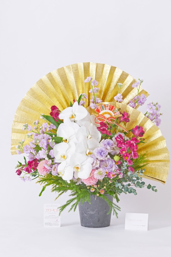 <p>大きな黄金の扇飾りと純白の胡蝶蘭が目に留まる、大切なお祝いに相応しい豪華な紫色系のアレンジメントフラワーです。</p>